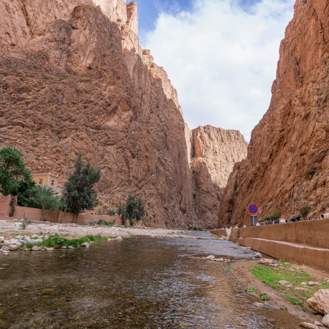 Eroded red rock cliffs tower over Todgha River in Todra Gorges, Morocco.