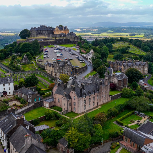 These images showcase Stirling Castle, one of the most important historic landmarks in Scotland, captured from above. The castle dominates Castle Hill and overlooks the surrounding town of Stirling and the Central Scotland countryside. With its strategic position, Stirling Castle played a key role in Scottish history, especially during the Wars of Independence. The surrounding area features stone buildings, winding streets, farmland, and the River Forth in the distance, blending urban and rural landscapes. This iconic fortress is not only a cultural treasure but also a popular travel destination that highlights Scotland’s medieval heritage and architectural legacy.